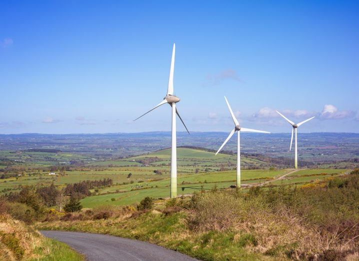 Three wind turbines in a rural area of Ireland against a clear blue sky.