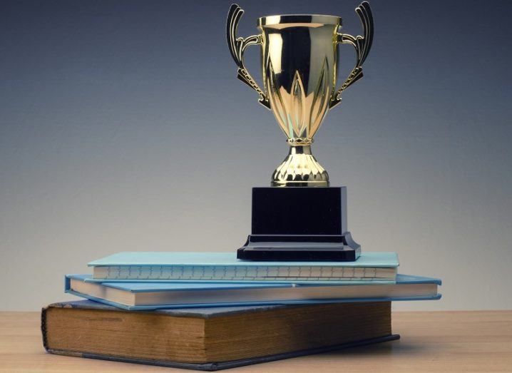 A gold trophy sitting on top of a pile of books on a wooden table.
