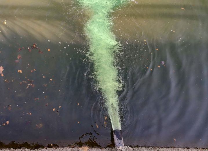 Aerial view of a pipe releasing green, polluted liquid into a river.