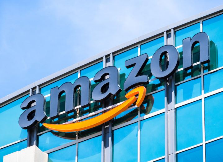 A large Amazon logo on the side of a glass building pictured on a clear, sunny day.
