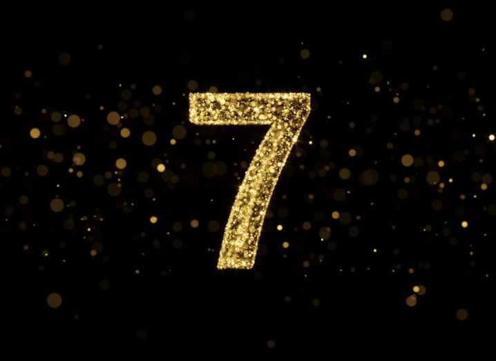 A number seven made of golden glitter on a black, sparkling background.