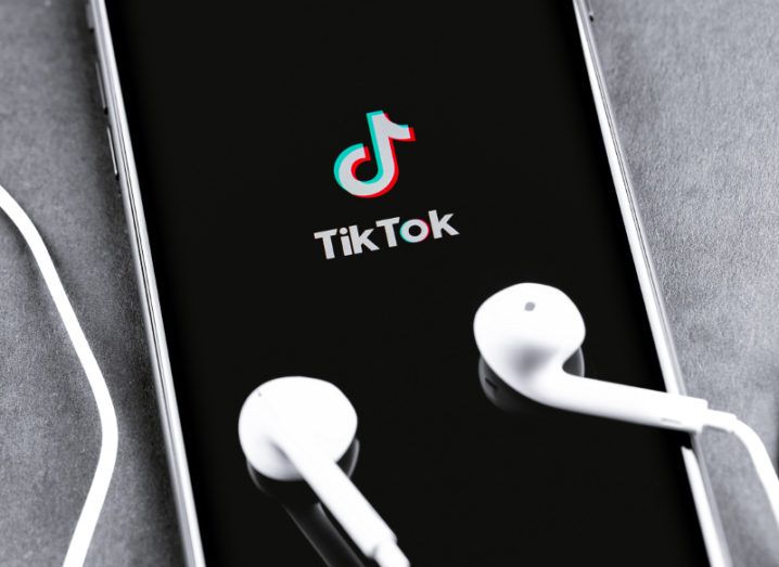 TikTok app logo on a black iPhone screen beside earphones.