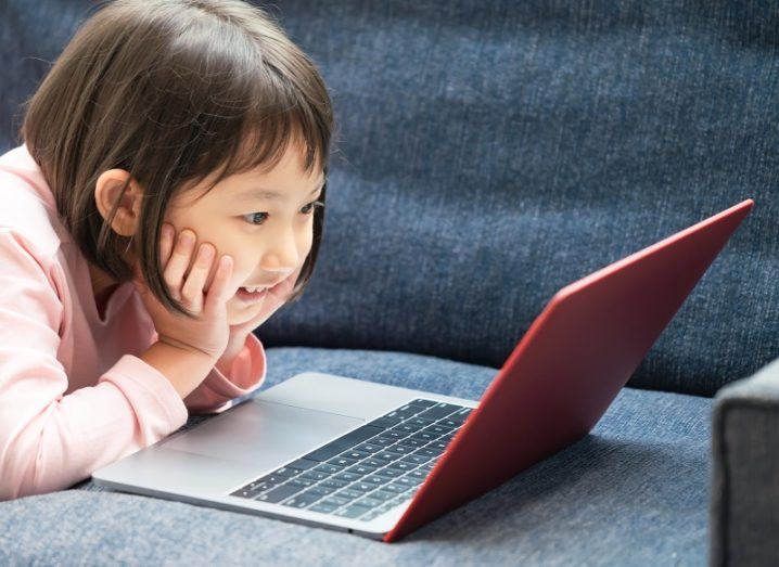 Young girl smiling and looking at a laptop screen.