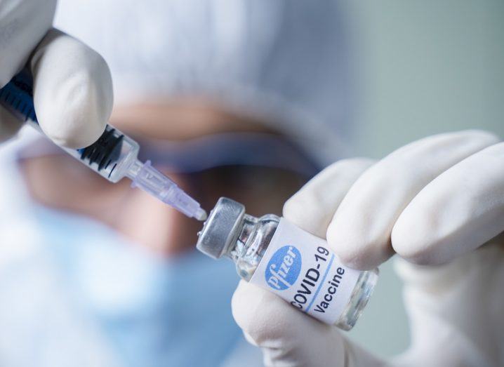 Doctor in full PPE putting a syringe in a vial of the Pfizer-BioNTech vaccine.