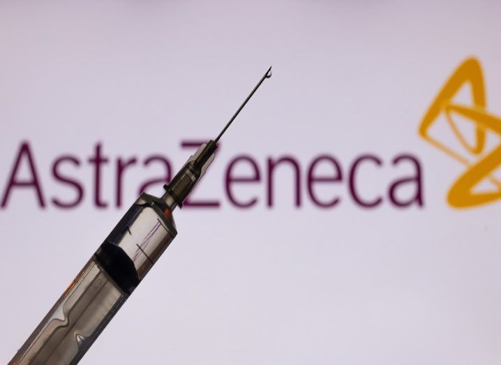 Syringe in front of an AstraZeneca logo on a white background.