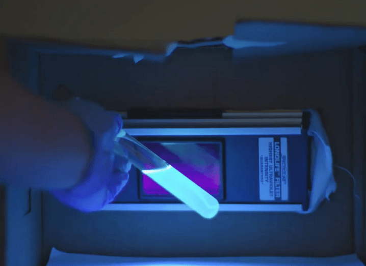 Blue luminescent liquid inside a test tube in front of the AuREUS material in a dark room.