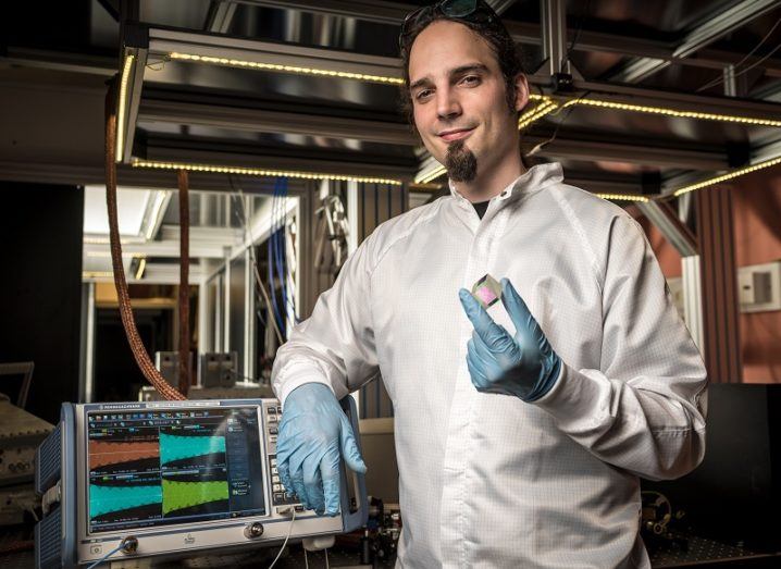 Klaus Jöns in a white lab coat smiling and holding a glass cube beside lab equipment.