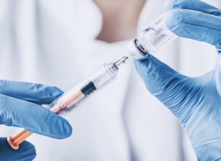 A close up of hands in blue gloves extracting a vaccine from a vile into a syringe.