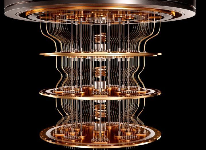 A gold quantum computer suspended from the air against a black background.