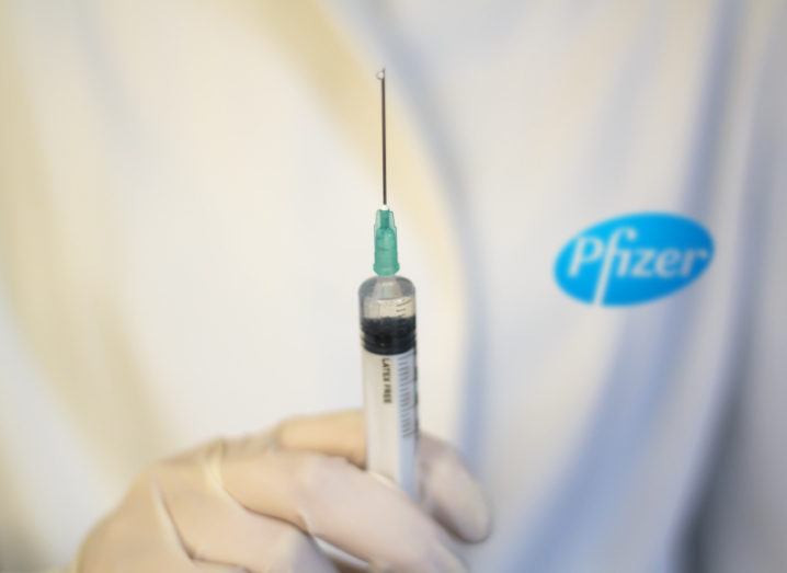 A person in a Pfizer lab coat holds a needle.