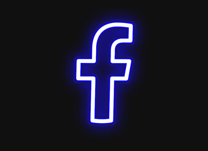 A neon blue light in the shape of the Facebook ‘F’ logo against a black background.