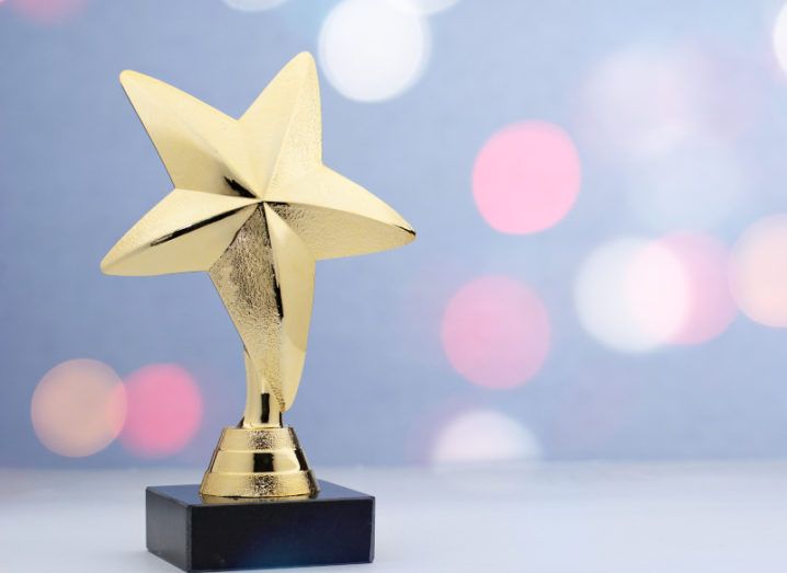 A gold trophy in the shape of a star against an out-of-focus blue background with faded pink lights.
