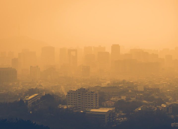 Aerial view of a city where pollution is obstructing visibility and an orange hue is cast across the area.