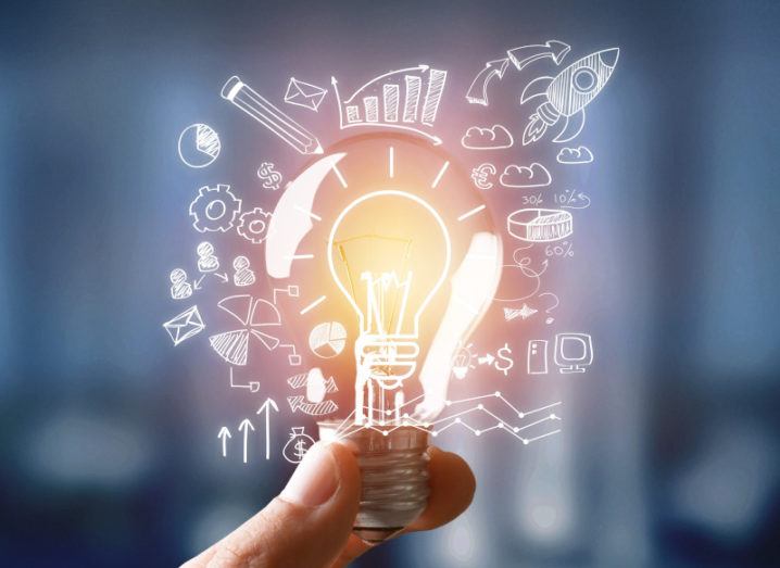 A hand is holding a lightbulb, surrounding by small graphics representing innovation and ideas.