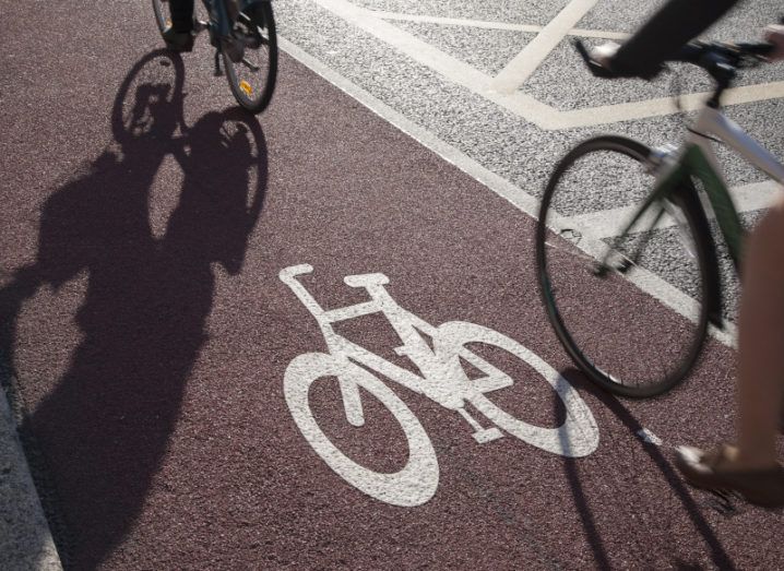 Two cyclists are going down a red cycle lane on the side of a Dublin road.