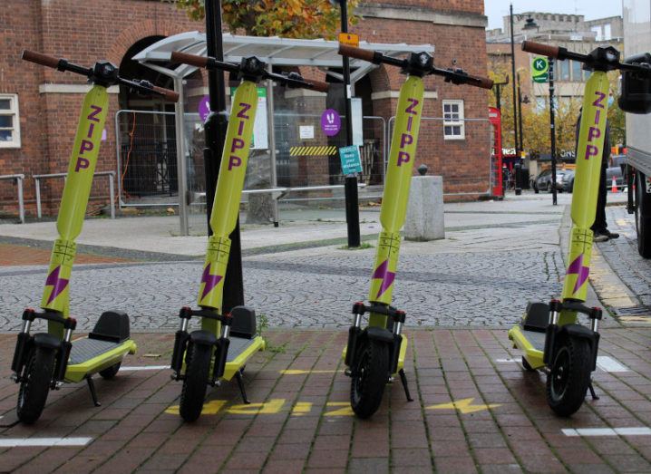 A row of yellow Zipp Mobility scooters are parked on a city street.