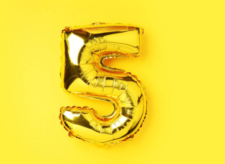 A large gold balloon in the shape of the number five against a bright yellow background.