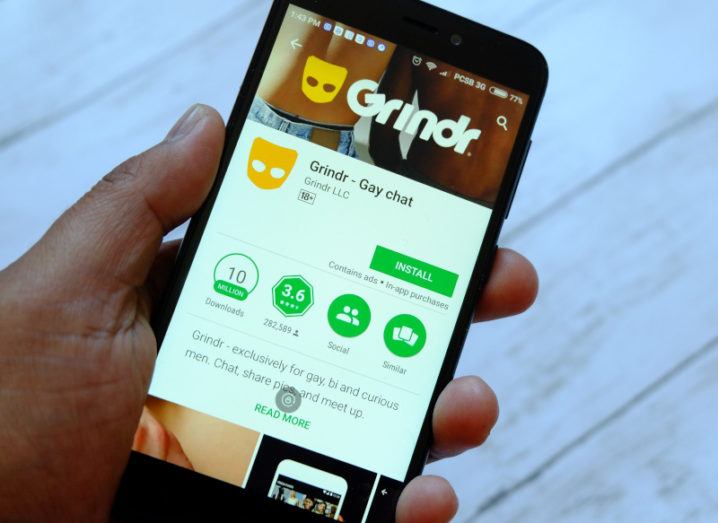 A hand holds a smartphone with the screen showing the installation page for the Grindr app.