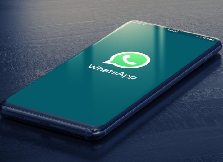 A smartphone lies on a dark wooden surface. The WhatsApp logo is displayed on the screen.