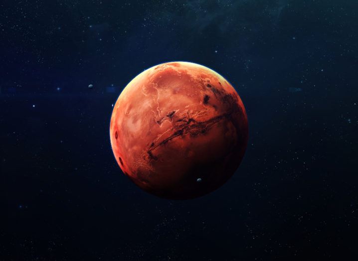 A red planet, half in light and half in shade, amid a dark background of stars.
