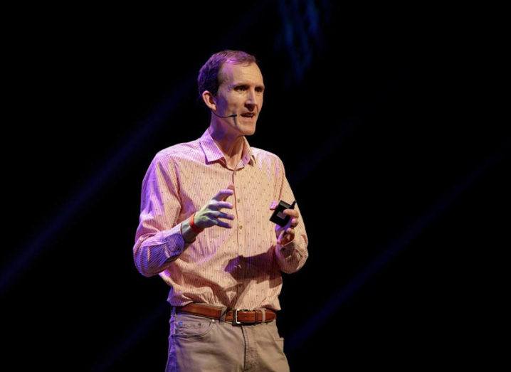 Gerry McGovern standing and speaking on stage against a dark background.