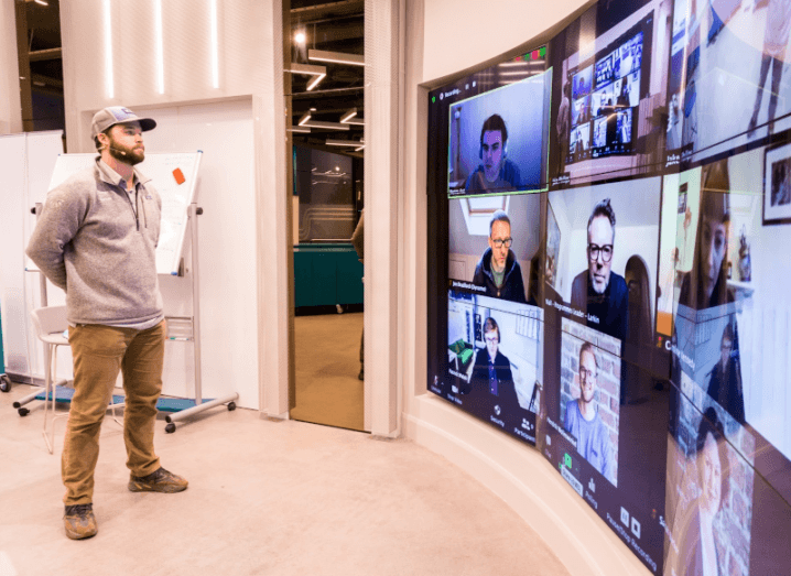 A man stands in Dogpatch Labs in Dublin, while speaking to a number of people on a large screen.