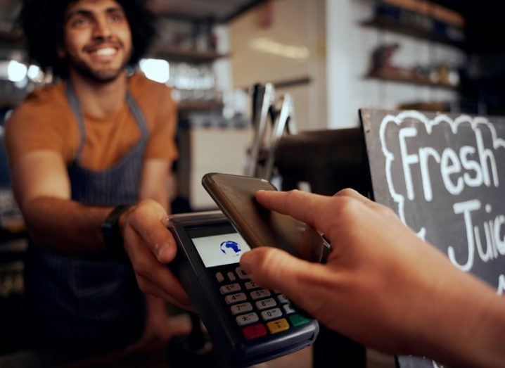 A person is making a contactless payment with their phone in a cafe.