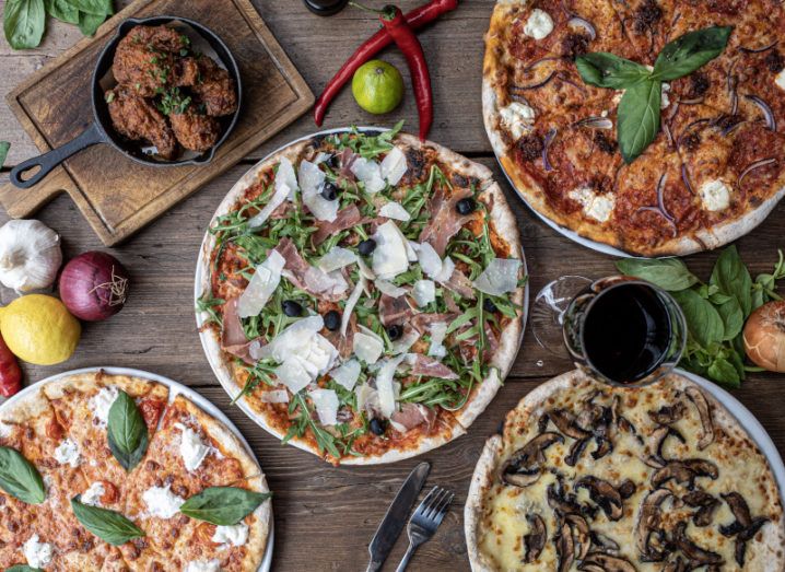 A bird’s-eye shot of a wooden table full of pizzas and other food that you might order from Just Eat Takeaway.