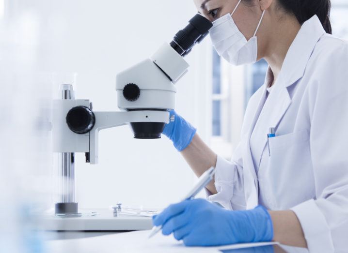 A woman researcher taking notes while looking through the microscope in a laboratory.