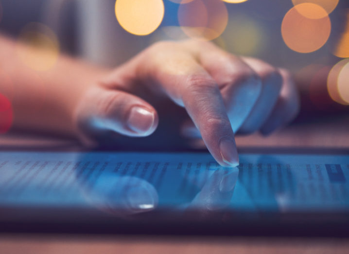 A person's finger is scrolling on a tablet in a darkened room, reading the news.