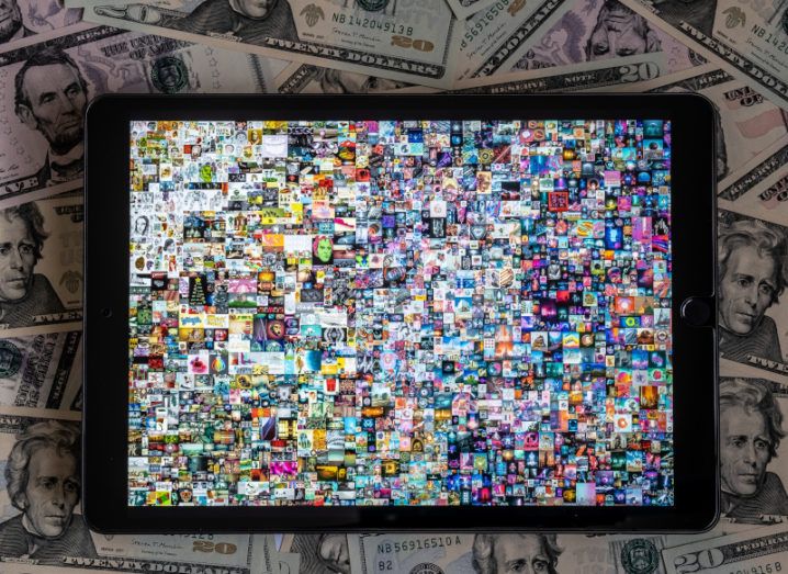A tablet displays the Beeple NFT artwork, which features many colourful squares of images. The tablet is sitting on a pile of money.
