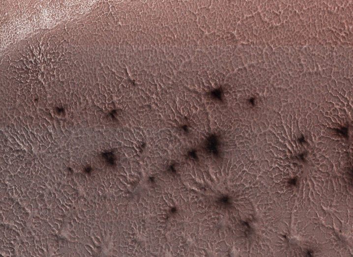 The red surface of Mars with dark topographic features that resemble spiders.