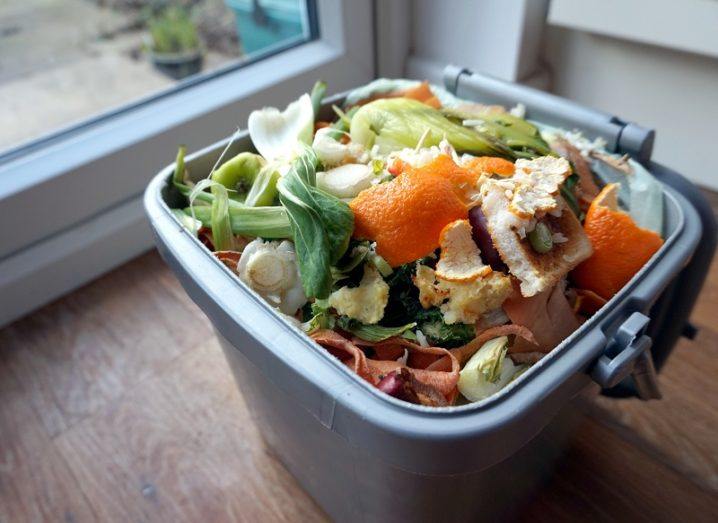 Container of domestic food waste sits on a wooden floor.