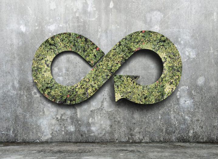 Green circular economy concept with a green infinity symbol against a grey stone wall.