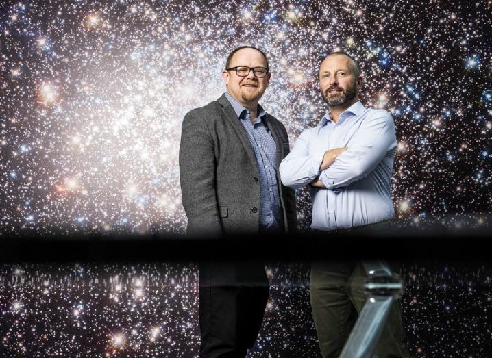 Two men stand against a starry background.