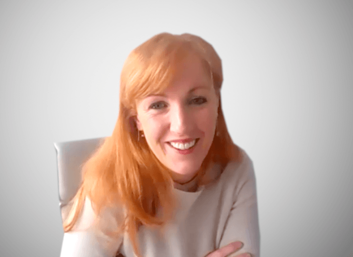 A screen shot of a woman with red hair smiling at the camera on a Zoom call.