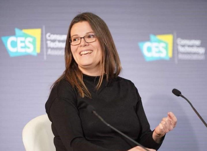 A woman with dark hair and glasses sits on a stage with the CES logo in the background.