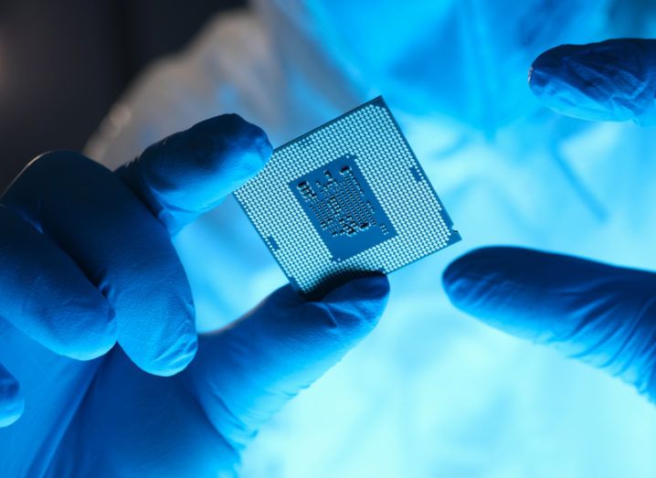 A close-up of gloved hands holding a semiconductor, representing the global chip shortage.