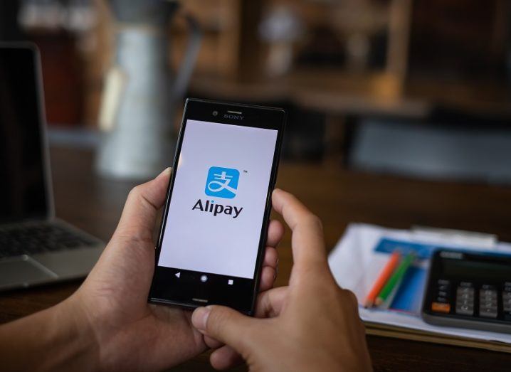 A person is holding a phone with the Alipay app open on the screen.