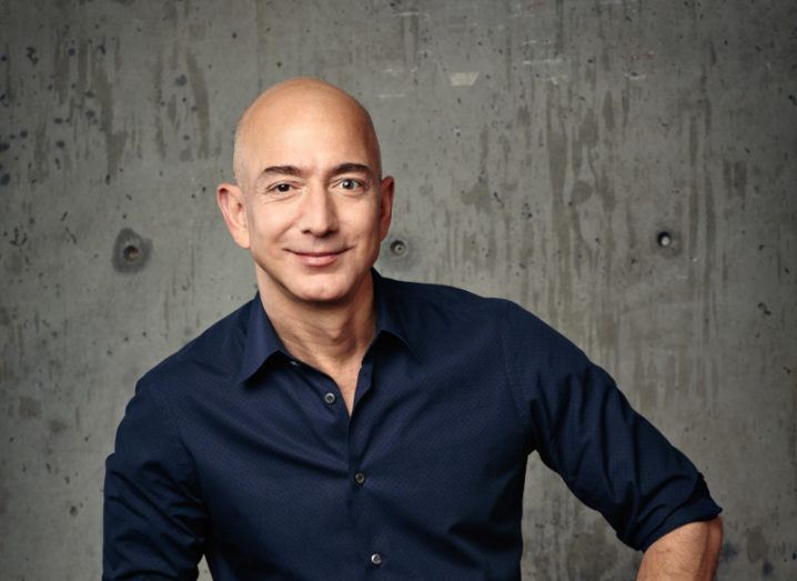 A head-shot of Amazon boss Jeff Bezos wearing blue shirt and sitting against a grey wall.