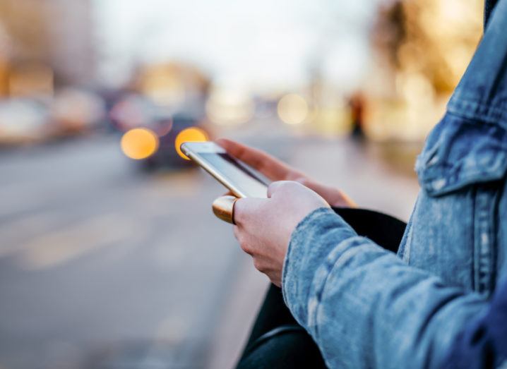 A close-up of a person holding a phone while standing beside a quiet road.