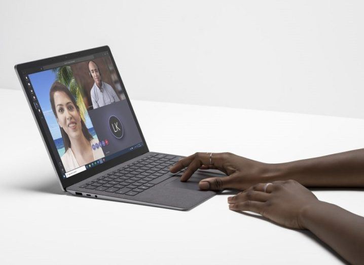 A man's hands are working on a Microsoft laptop, against a plain white surface.