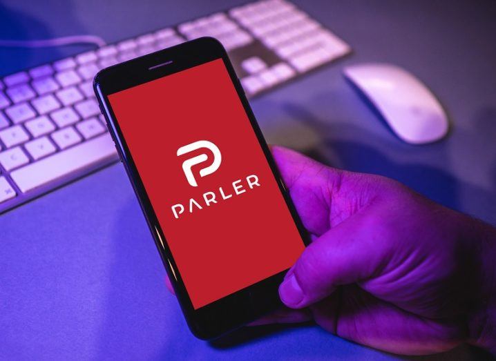 A man’s handing is holding a phone with the Parler app open on the screen.