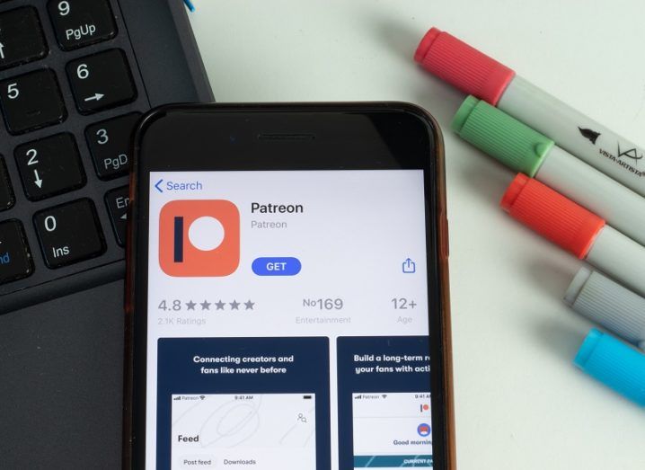 The Patreon app is open on a mobile phone screen. The phone is sitting on a desk beside a keyboard and some coloured markers.