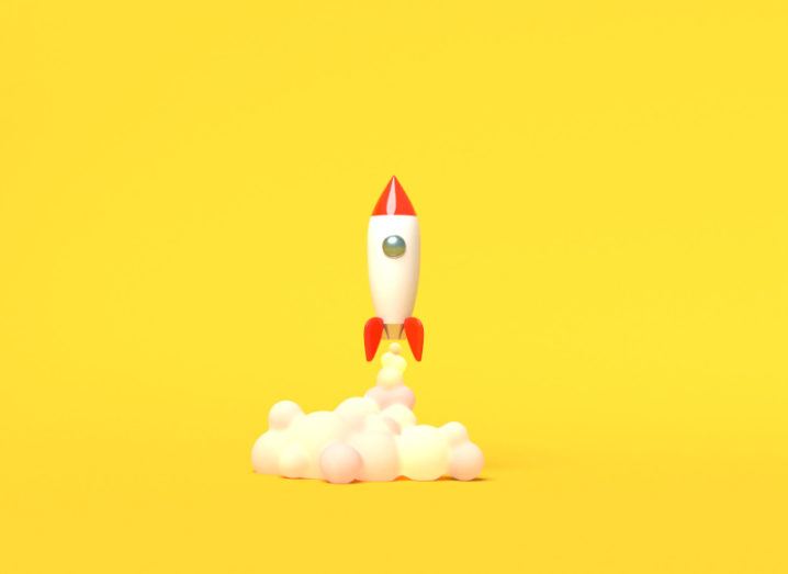A toy rocket is taking off against a yellow background.