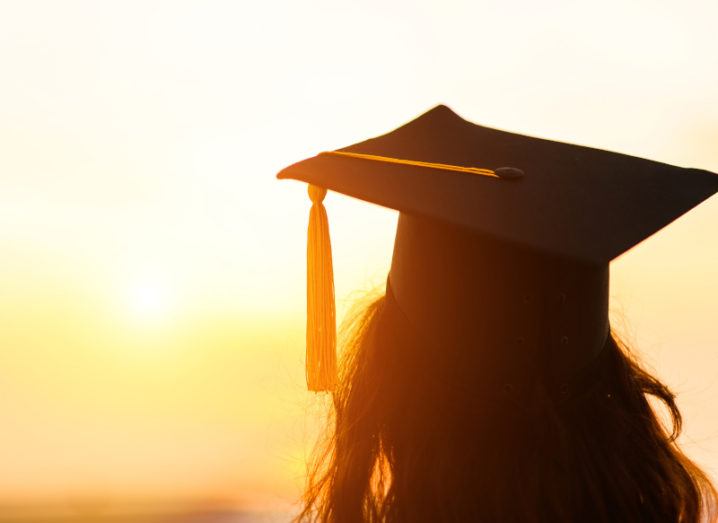 Silhouette of a person wearing a graduation cap and staring into the sunset.
