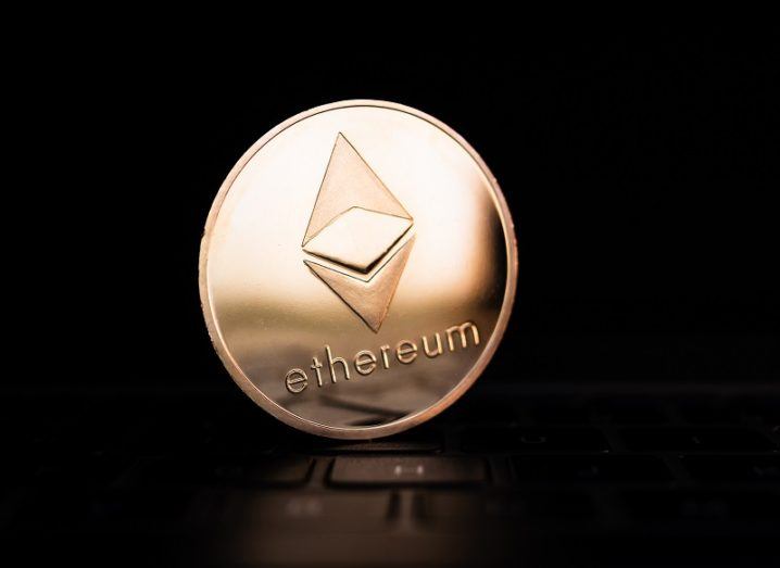 A golden coin with the Ethereum logo on it is sitting on a computer keyboard against a dark background.