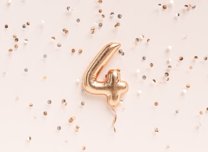 A rose gold balloon shaped like the number four against a soft pink background dotted with rose gold confetti.