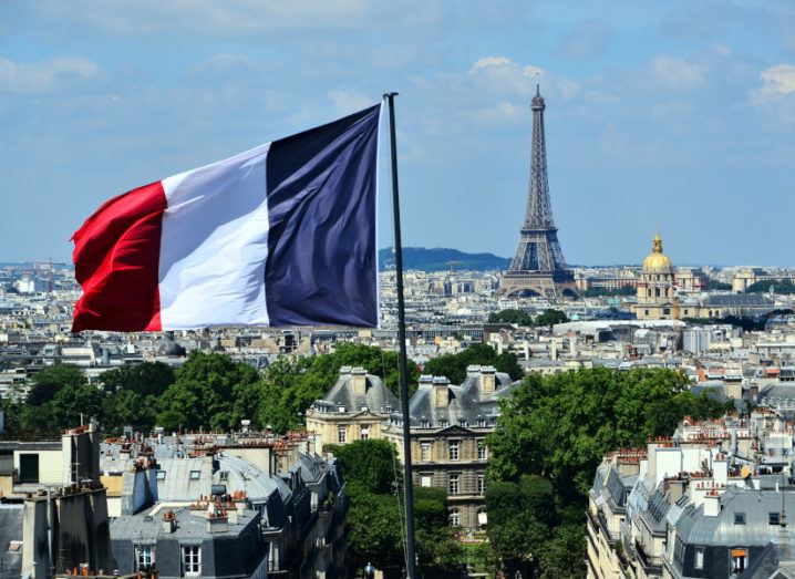 Rooftop view of the city of Paris, taking in the Eiffel Tower and a large French flag flying in the foreground.