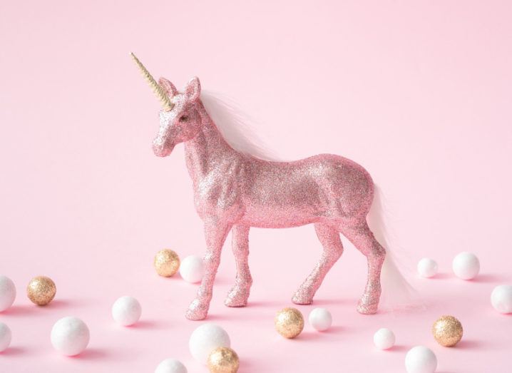 A pink, glitter-coated model of a unicorn stands among a scattering of white and gold spheres.